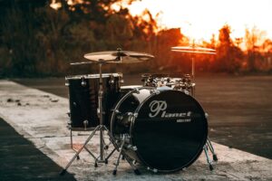 Photo by Ingridi Alves Photograph black Planet drum kit near trees during sunset